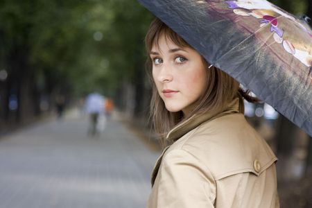 Yong woman with umbrella walking along the avenueの写真素材