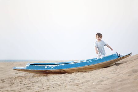 little boy standing in the boat lying on the beachの写真素材