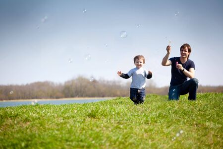 happy dad and his son playing together in the nature with soap bubblesの写真素材