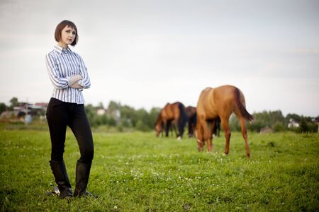 young horse woman standing in the field and 2 horses on backgroundの写真素材
