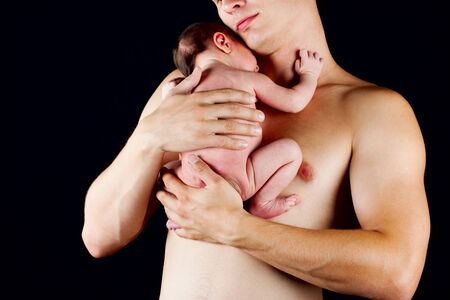 young father holding his newborn son carefully over blackの写真素材