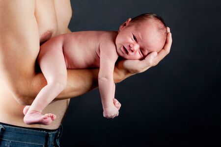 young father holding his newborn son carefully over blackの写真素材