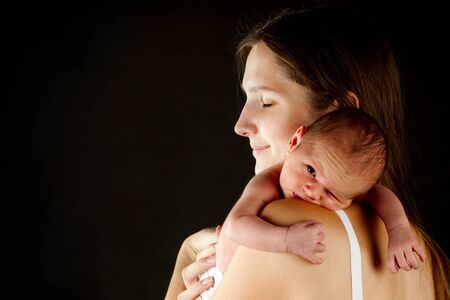 young happy mother holding his newborn boy over blackの写真素材