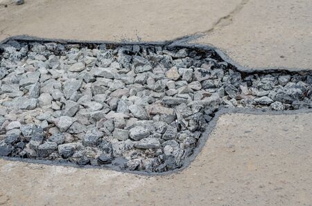 Hole in the asphalt road. The edges of the pit are treated with resin. Repair asphalt road pavement hole and laying new asphalt patching method outdoors. Selective focus. Without anyone.の写真素材
