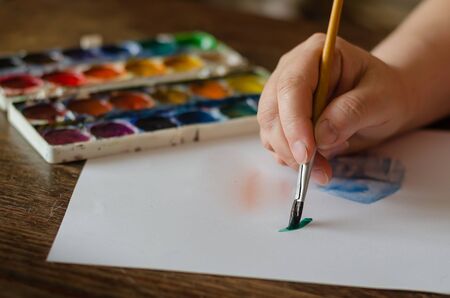 Brush with green paint in the right hand. Creation of a creative drawing. Selective focus. Eye level shooting. Close-up.の写真素材