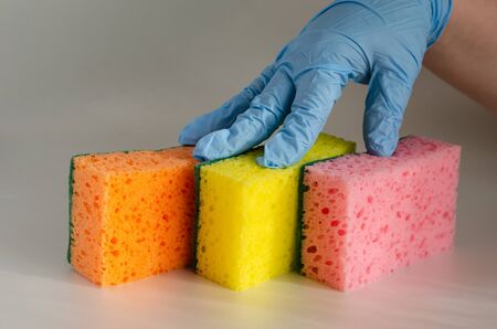 Fingers in a protective glove press new sponges to the table. Commercial cleaning company or home economics. Side view. Selective focus.の写真素材