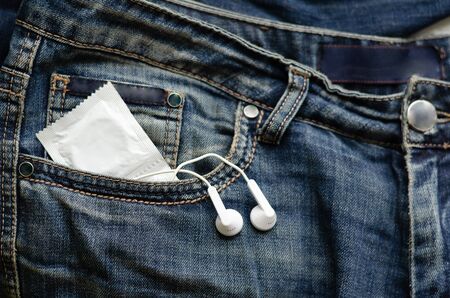 Two condoms in a package and portable headphones are visible from the jeans pocket. Close-up. Selective focus. Landscape photo location.の写真素材