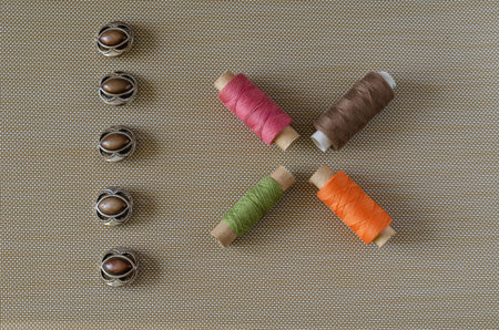A line of buttons and spools of thread. Five brown buttons. Four multi-colored spools of thread....