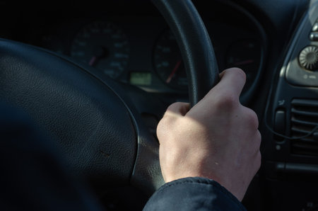 Taxi driver's right hand on the steering wheel. A young taxi driver holds the wheel while driving in...