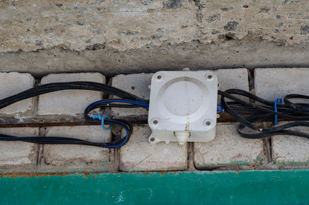 Open wiring on a brick wall. Wires in black insulation are included in the plastic junction box. Shooting outdoors. Selective focus.の写真素材