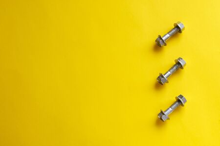 Nuts and bolts on a yellow background. Composition and three bolts with nuts. Free space on the left. Abstract multitask background. View from above. Selective focus. Close-up.の写真素材