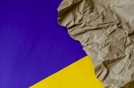 Brown paper on a yellow-blue background. A piece of crumpled paper with torn edges. Abstract background. Top view at an angle. Selective focus. Close-up.の写真素材