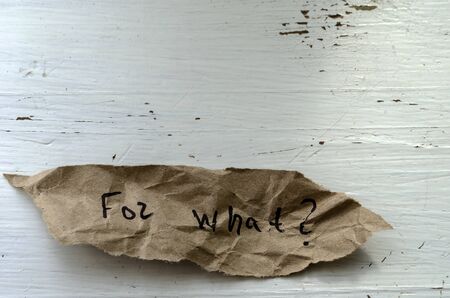 For what Question written by hand on a piece of torn paper. A scrap of paper on a wooden background. Shooting from above at an angle. Selective focus. Close-up.の写真素材