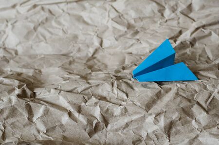 Blue paper plane on a beige background. Crumpled wrapping paper simulates air currents. Travel and tourism concept. Selective focus. Close-up.の写真素材