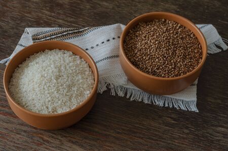 Rice and buckwheat in bowls. Two clay bowls with dry cereals. Traditional food. Top view at an angle. Wooden background with scratches and cracks. Selective focus.の写真素材