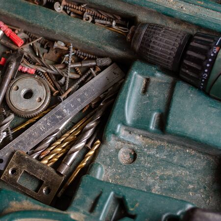 Old toolbox with a drill and drills. Ruler, screws, drills and power drill in a green box. Top view at an angle. Selective focus. Close-up.の写真素材
