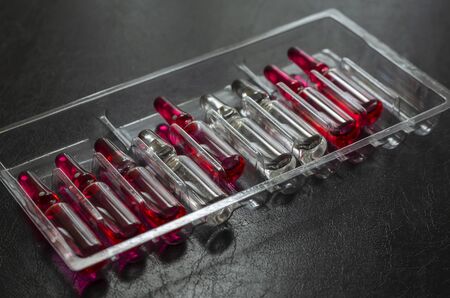 Multi-colored ampoules with medicines on a dark background. Glass ampoules with vitamins B1, B6 and B12 in a plastic tray. Therapeutic course of vitamins to enhance immunity. Selective focus. Close-upの写真素材