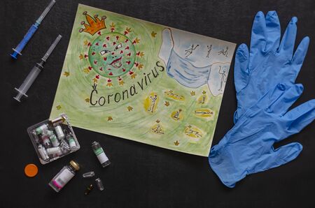 Drawing on paper coronavirus. Children's drawing on a black table next to protective gloves, syringes and ampoules. Top view at an angle. Selective focus.の写真素材