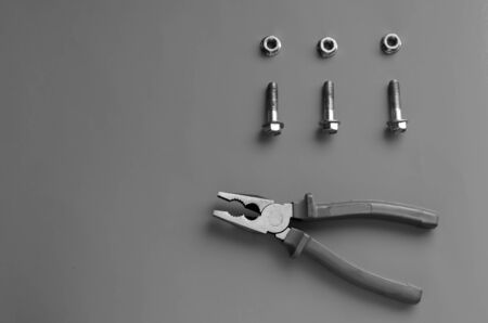 Pliers and bolts. Composition of hand tools with blue handles and three bolts with nuts. View from above. Selective focus. Monochromeの写真素材