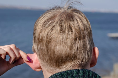 The girl’s fingers are pulling the boyfriend’s ear. Hand of a young girl with multi-colored...