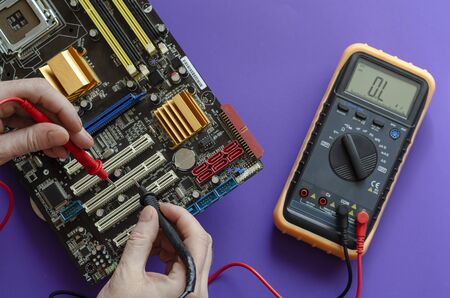The process of repairing the motherboard. Checking the electrical resistance of the motherboard. Hands using a digital multimeter to test. View from above. Selective focus. Close-upの写真素材