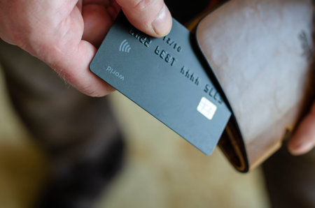 Hand takes out a bank card from the wallet. Adult man holds a black bank card. Payment for goods in...