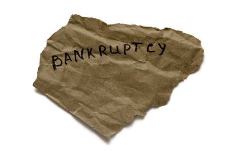 A scrap of torn paper with the word bankruptcy. Handwritten inscription on brown paper. Isolate on a white background with shadow. View from above. Big plan.の写真素材