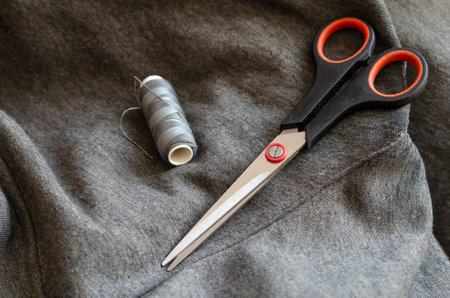 Spool of gray thread with a needle and scissors. Tailor's manual tool on gray fabric. Craft tailor...