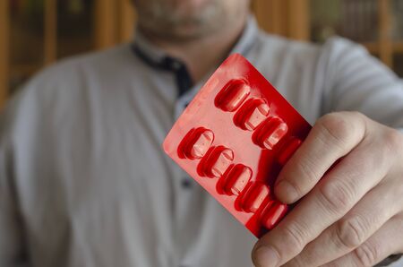 A man holds out a blister with pills. The hand of an adult male in the camera holds out pills. The concept of sexual health in men. Focus in the foreground. Blurred background.の写真素材