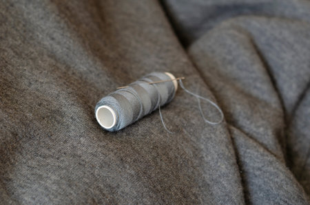 Spool of gray thread with a needle. Tailor's manual tool on gray fabric. Craft tailor or seamstress....