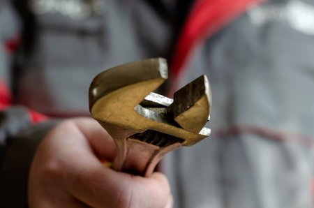A man holds out an adjustable wrench into the camera. Mechanic in a red-gray working uniform with a...