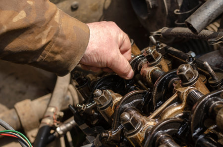 Checking the thermal clearances of the intake valves of the gasoline engine. An elderly mechanic...