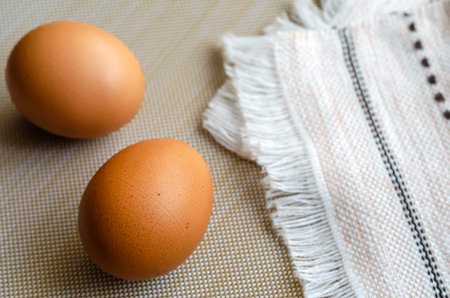 Two brown chicken eggs and a kitchen towel. Closeup of uncooked farm eggs on beige. A folded towel...