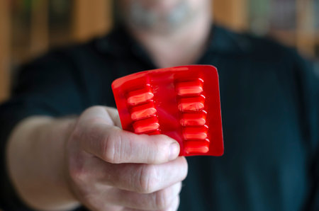 A man holds out a blister with pills. The hand of an adult male in the camera holds out pills. The...