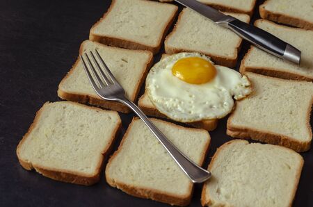 Ready to eat chicken egg on bread. Fried eggs and fork with a knife on slices of bread for sandwiches. Angled side view. Selective focus.の写真素材