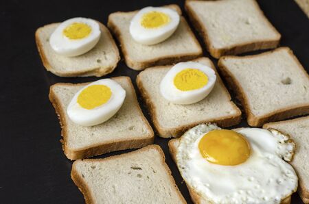 Ready-to-eat chicken eggs on bread. Fried eggs and halves of boiled eggs on pieces of bread for sandwiches. Angled side view. Selective focus.の写真素材