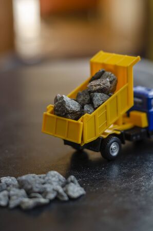 Yellow Plastic Model Toy Truck. Imitation of unloading crushed stone from the body. A stack of rubble in the foreground. Construction topics. Selective focus.の写真素材