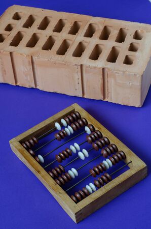 Brick and wooden abacus on a blue background. New red brick and screw wooden abacus. Construction topics. Close-up. Selective focus.の写真素材