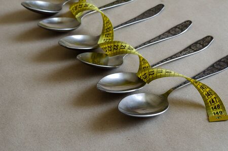 Metal spoons and tailor meter. A line of six cutlery and a yellow meter. Overweight, overeating. Side view. Selective focus.の写真素材