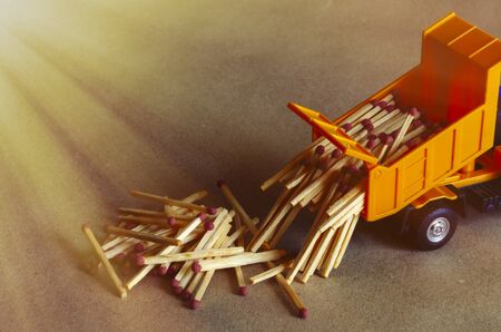 A yellow toy dump truck spills matches. A toy truck unloads a full body of wooden matches. Creative industrial background. Logistic topics. Selective focus.の写真素材