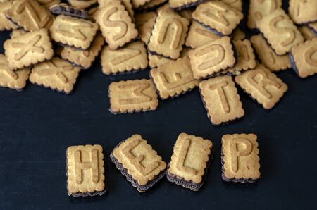 From capital letters the word HELP is laid out. A lot of cookies alphabet nearby. Focus in the foreground. Copy space. Close-up.の写真素材