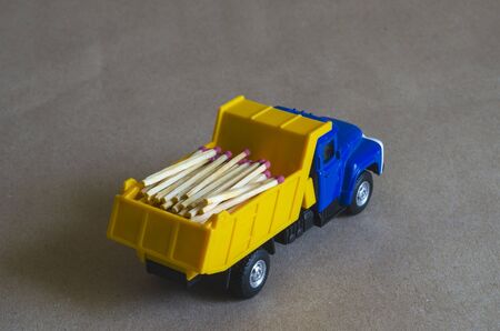 A yellow dump truck with a blue cab carries matches. Toy truck with a full body of wooden matches. Creative industrial background. Logging and logistics. Selective focus.の写真素材