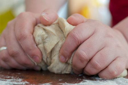 Female hands knead the dough on the kitchen table. Closeup of the hands of an adult woman with a large piece of dough. The process of making homemade meat dumplings. Homemade food.の写真素材