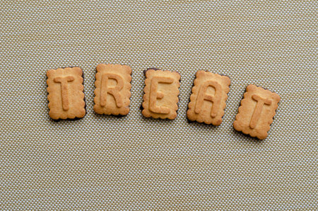The word TREAT is a cookie alphabet. Single word on a beige background. View from above. Close-up.
