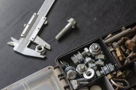 Caliper and Box with bolts and nuts. Choosing the right metal fastener. Use of manual measuring instruments. Focus in the foreground. Close-up.の写真素材