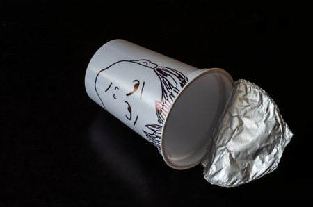A plastic glass with foil lid and pictured face of a perplexed person. A grimace of surprise...