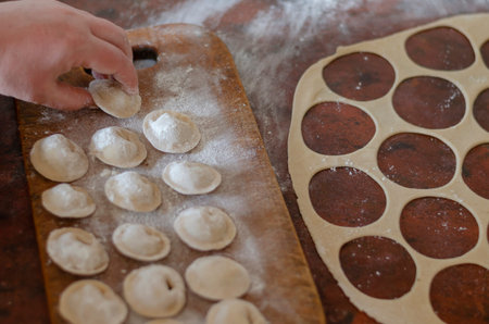 Female hand lays raw homemade dumplings. Serving of dumplings with meat on a wooden cutting board....
