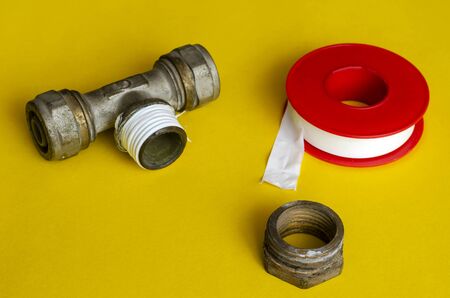 Water tee splitter, nut and sealing tape on a yellow background. The process of repairing the water supply. Plumber or plumbing service. Close-up. Selective focus.の写真素材