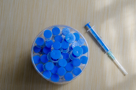 Many used syringes in a plastic jar. Blue medical syringes in a round container on the table....