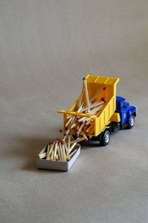 A yellow toy dump truck spills matches. A toy truck unloads a full body of wooden matches. Creative industrial background. Logistic topics. Selective focus.の写真素材